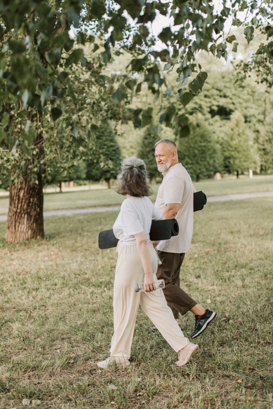 Older couple walking through a park with yoga mats